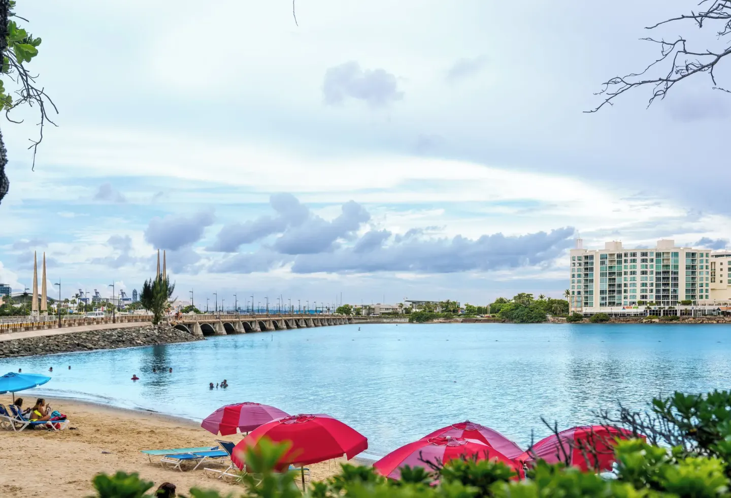 Sandy beach with umbrellas and calm lagoon water at The Condado Plaza Hotel.