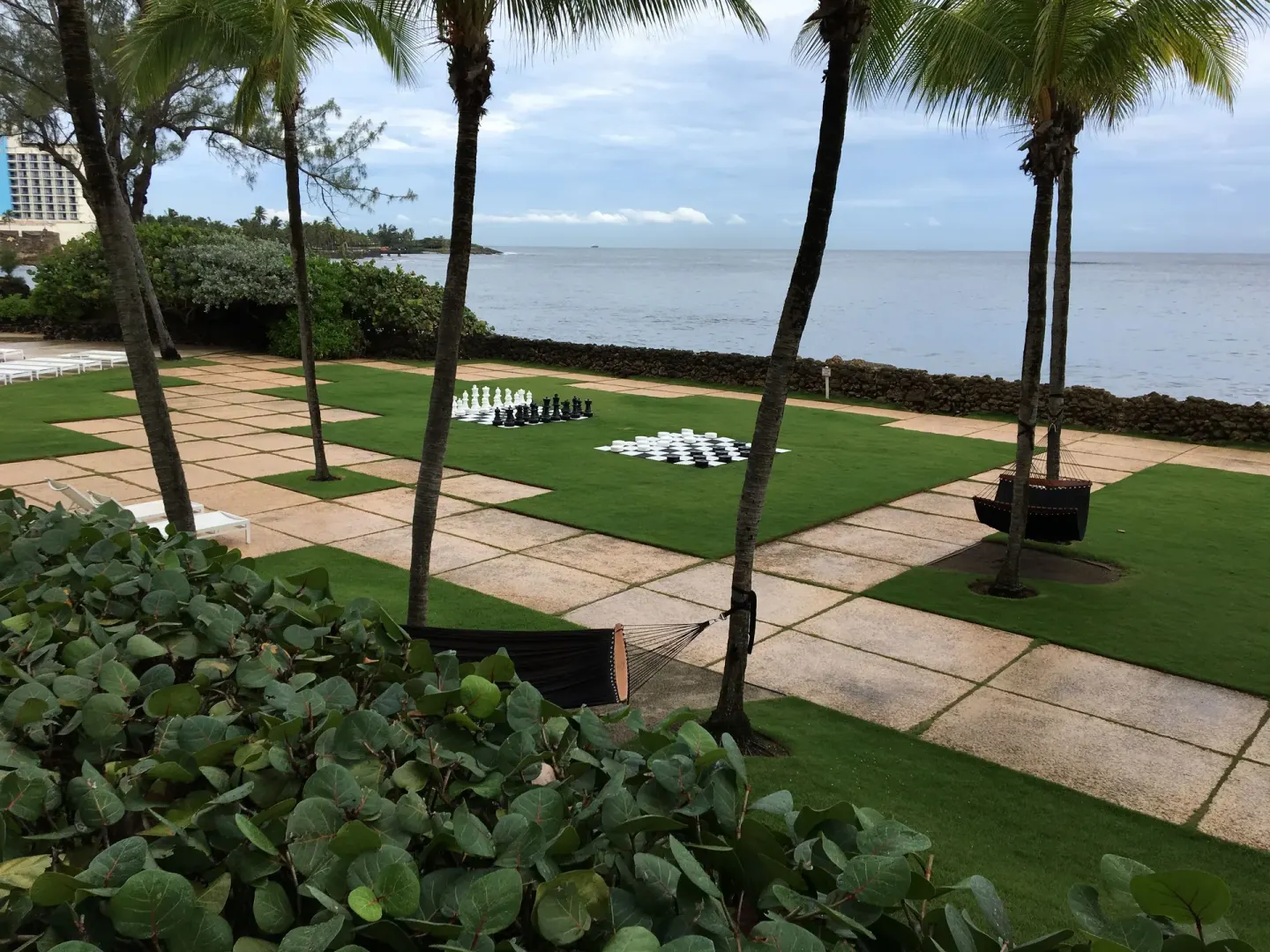 Oceanfront lawn at The Condado Plaza Hotel with palm trees, hammocks, and oversized chess sets.