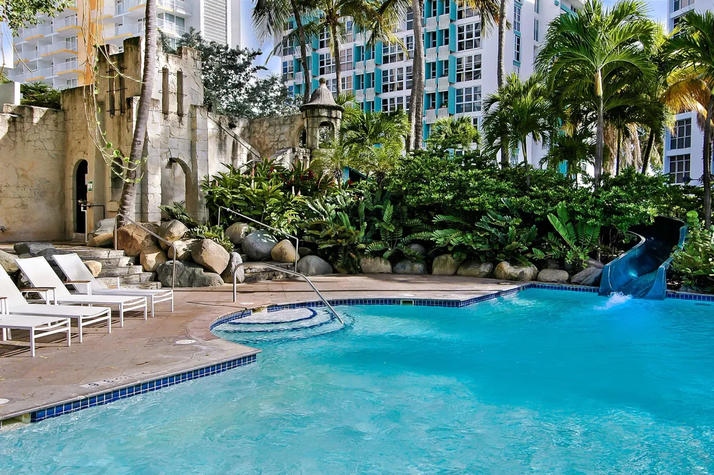 Pool with a waterslide and tropical landscaping at The Condado Plaza Hotel.