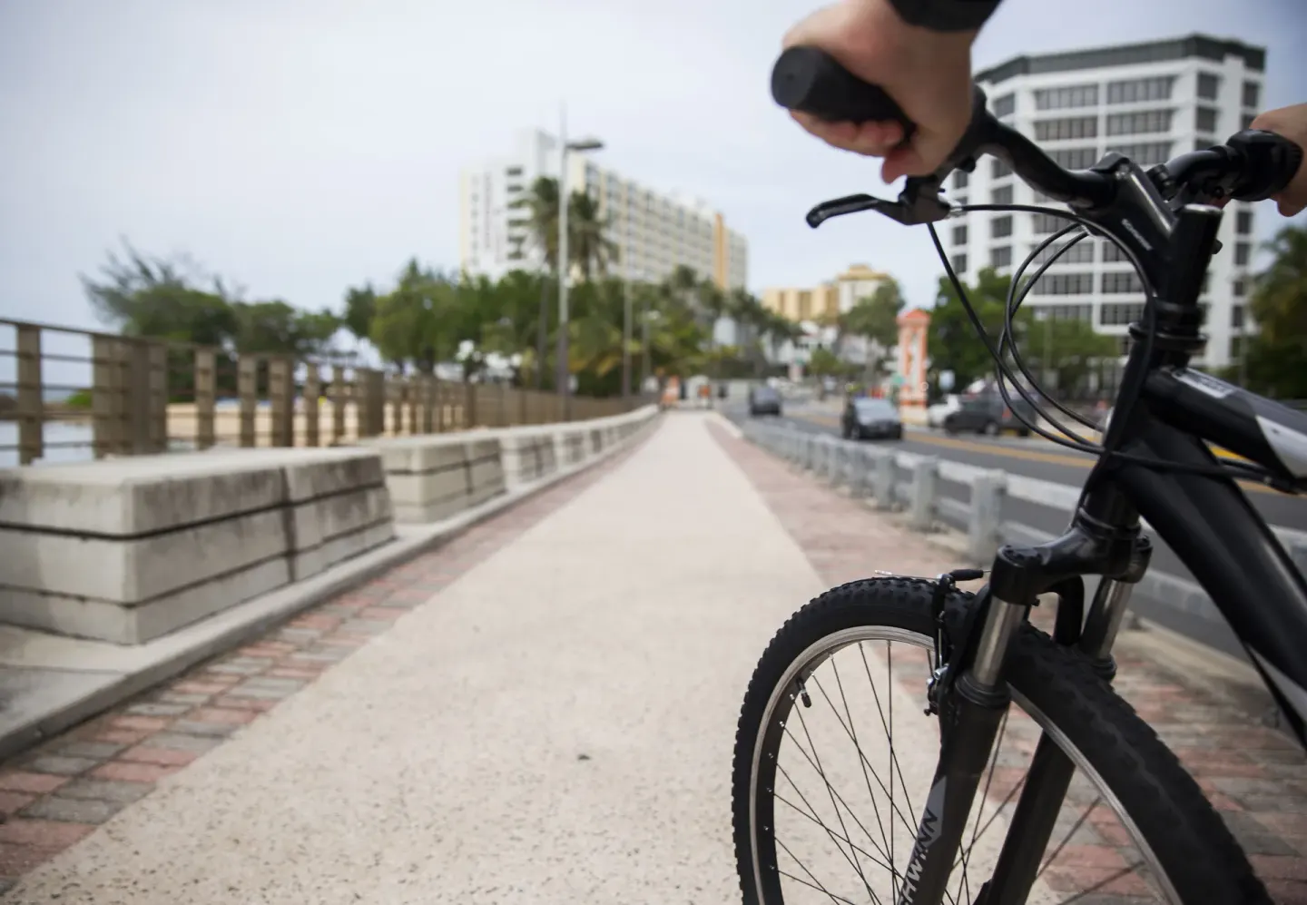 Cyclist holding a bike on a waterfront path near The Condado Plaza Hotel.