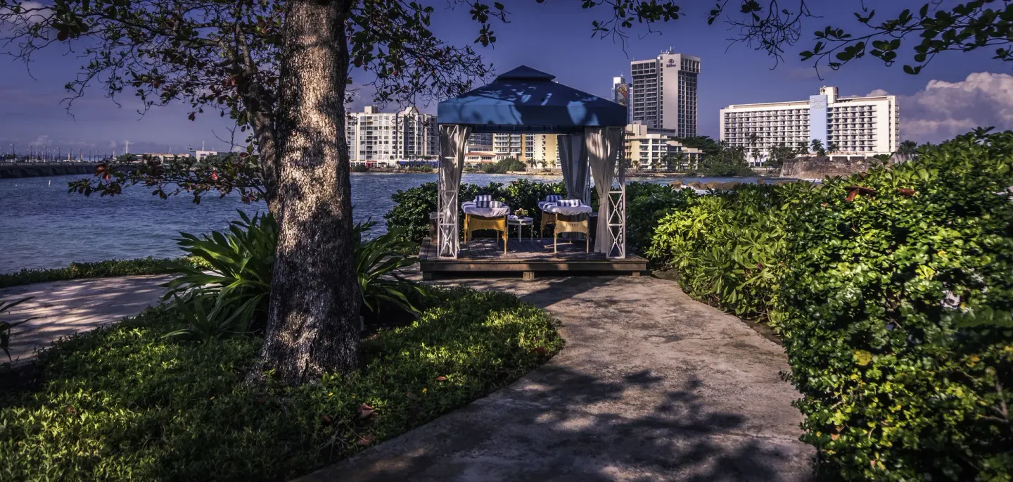 Waterfront gazebo set for dining at The Condado Plaza Hotel with bay and city buildings beyond.