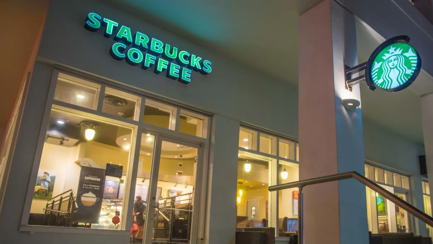 Illuminated Starbucks entrance at The Condado Plaza Hotel with windows and visible café interior.