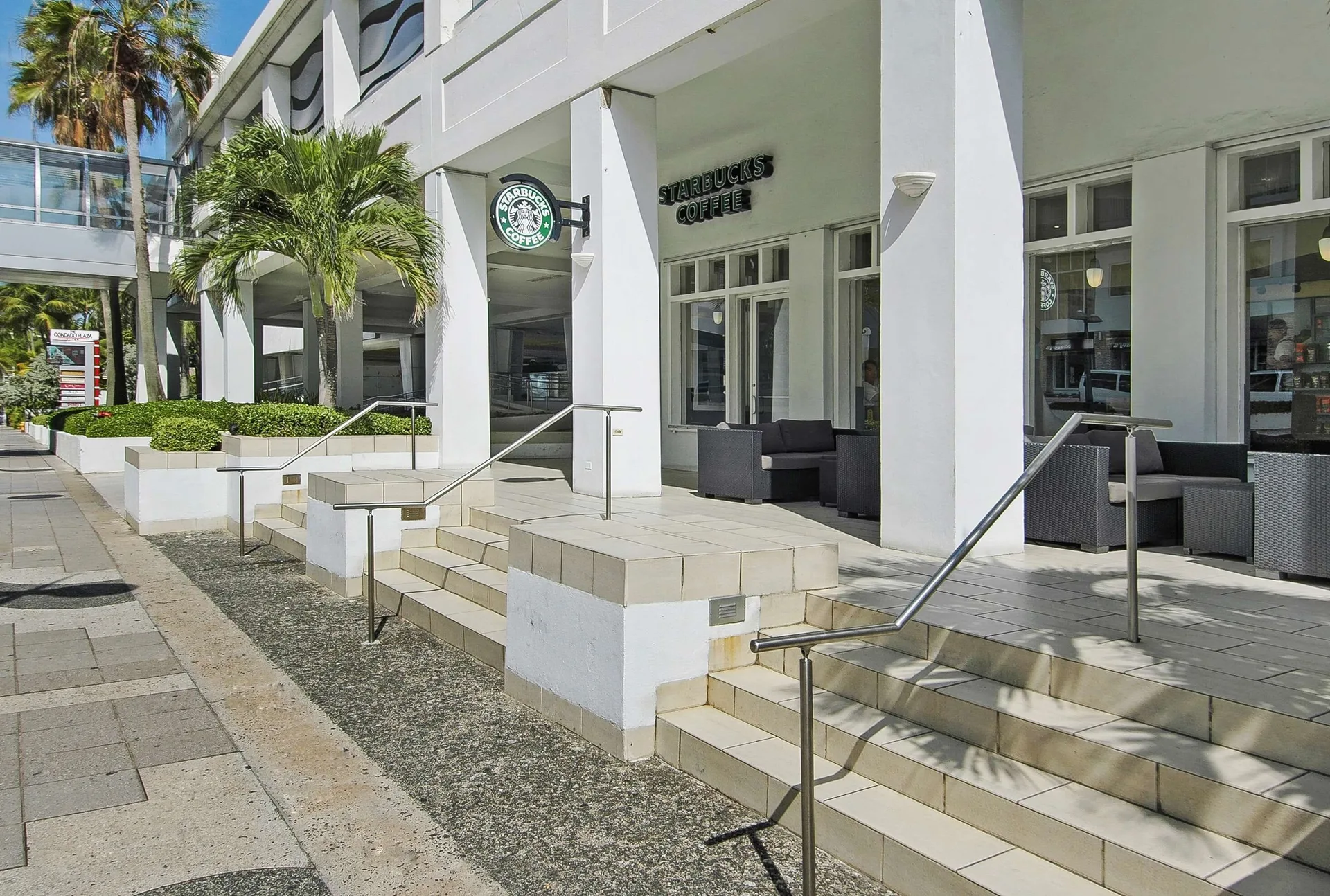 Starbucks exterior at The Condado Plaza Hotel with steps, patio seating, and palm landscaping.
