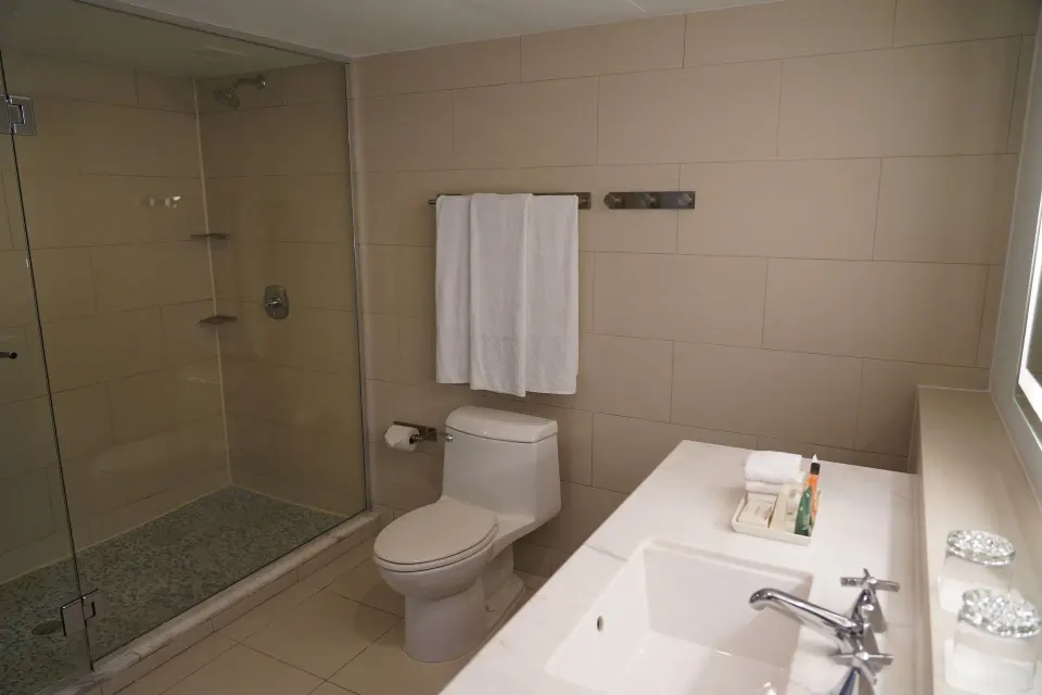 Deluxe Room bathroom with glass shower, toilet, vanity, and towels at The Condado Plaza Hotel.