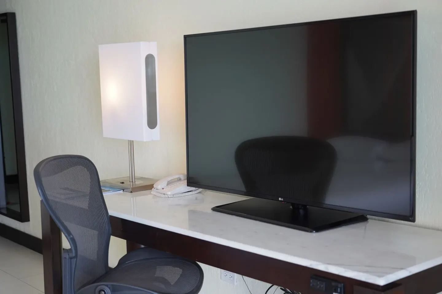 Desk with TV, lamp, phone, and mesh chair in a Deluxe Room at The Condado Plaza Hotel.