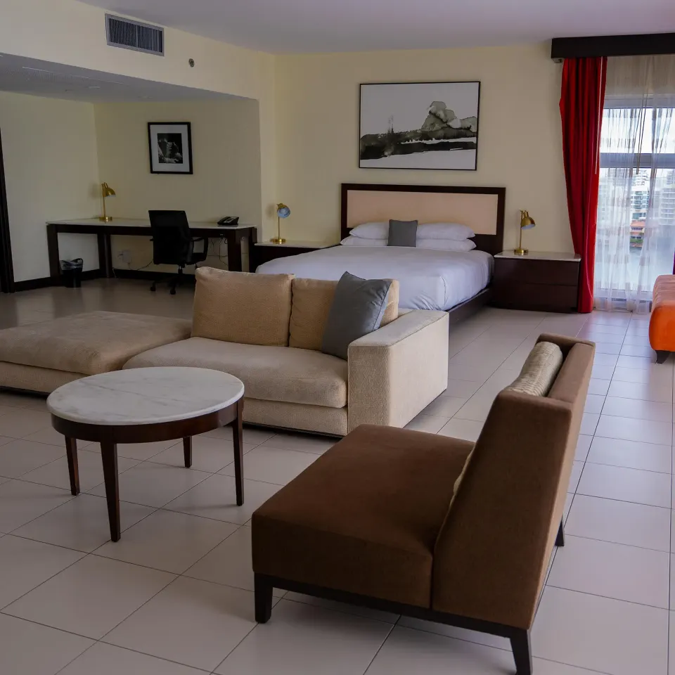 Junior Suite balcony room with king bed, seating area, desk, and red curtains at The Condado Plaza Hotel.