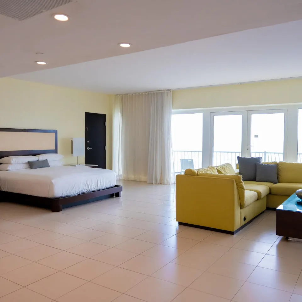 Junior Suite balcony with king bed, yellow sofa, and balcony doors at The Condado Plaza Hotel.