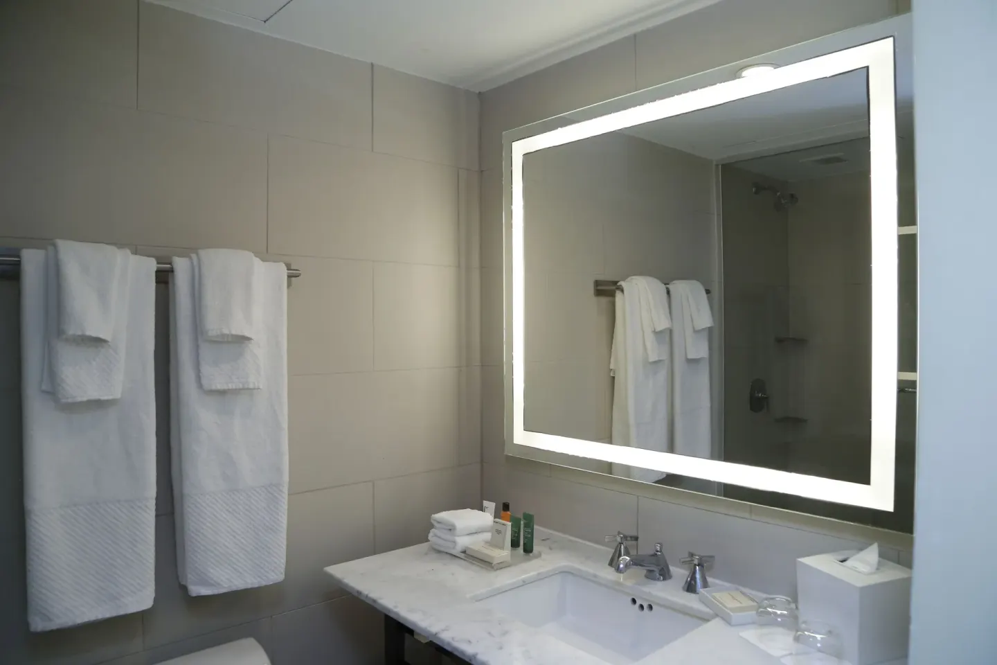 Accessible bathroom vanity with lit mirror, towels, and shower reflection at The Condado Plaza Hotel.