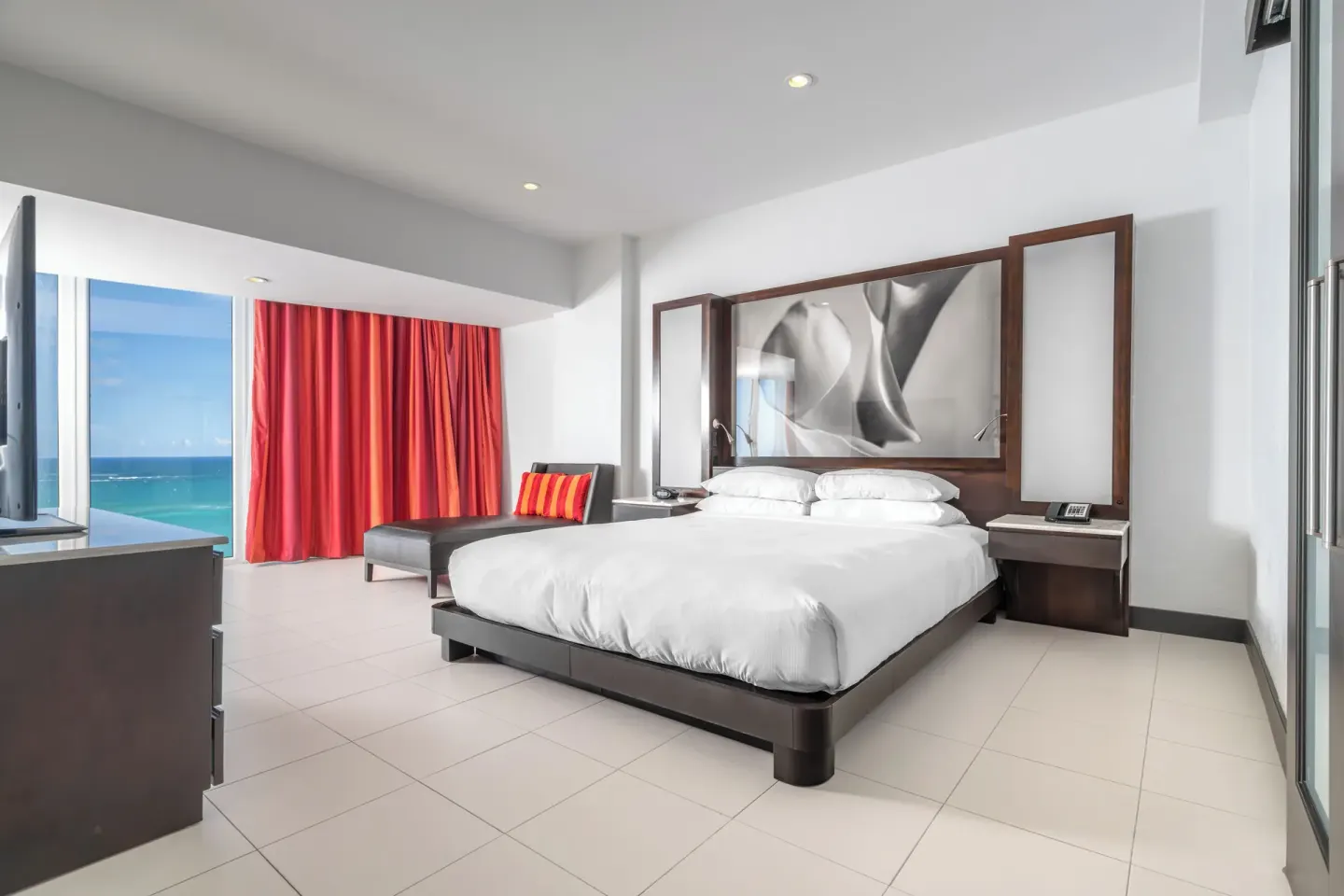 Ocean-view guest room with king bed, chaise, and red curtains at The Condado Plaza Hotel.