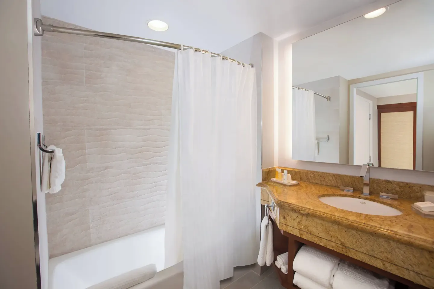 Guest bathroom with tub, curtain, and stone vanity at The Coral at Atlantis.