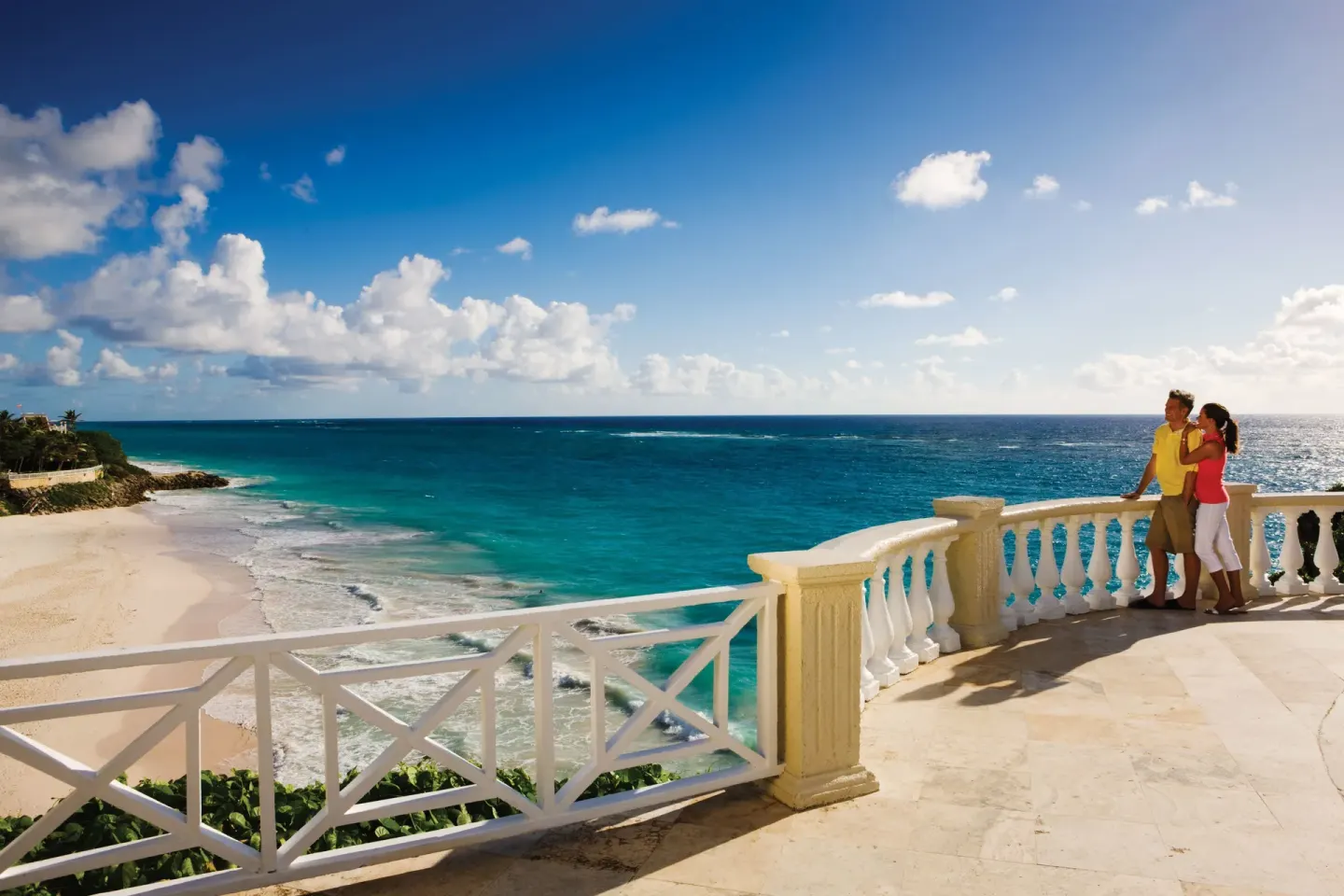 A couple stands at a cliffside railing above The Crane Resort at The Crane Resort.