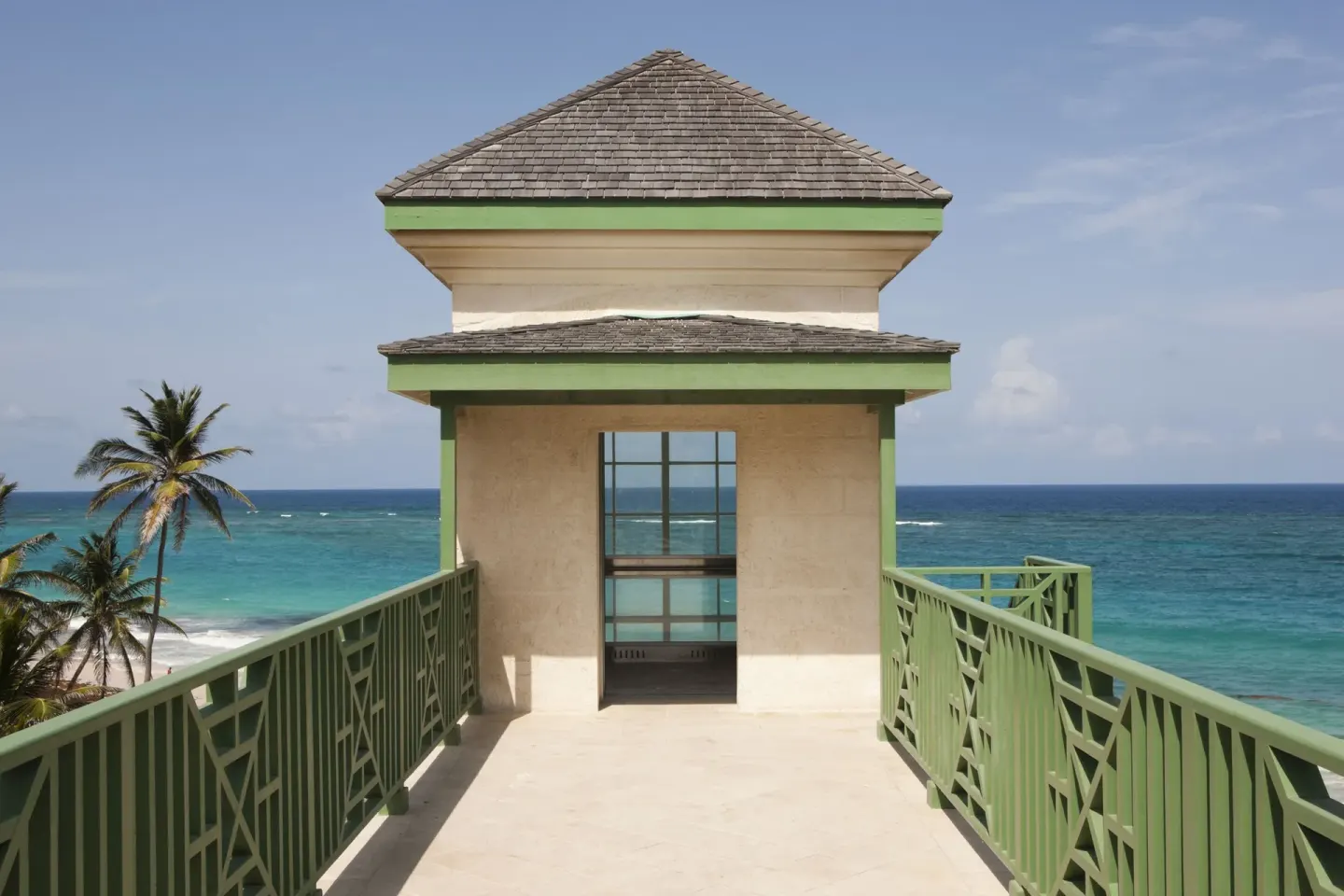 A green-railed oceanfront walkway leads to a pavilion at The Crane Resort.
