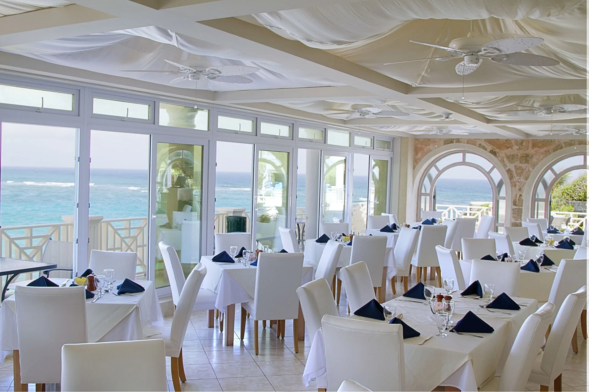 Ocean-view dining room with white tables and arched windows at The Crane Resort.
