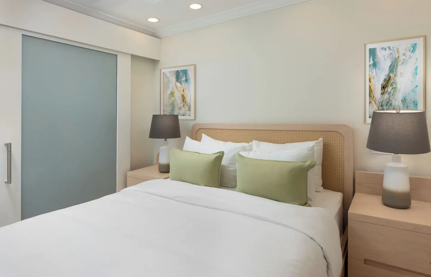 King bed with woven headboard, bedside lamps, and abstract art at The Crane Resort.