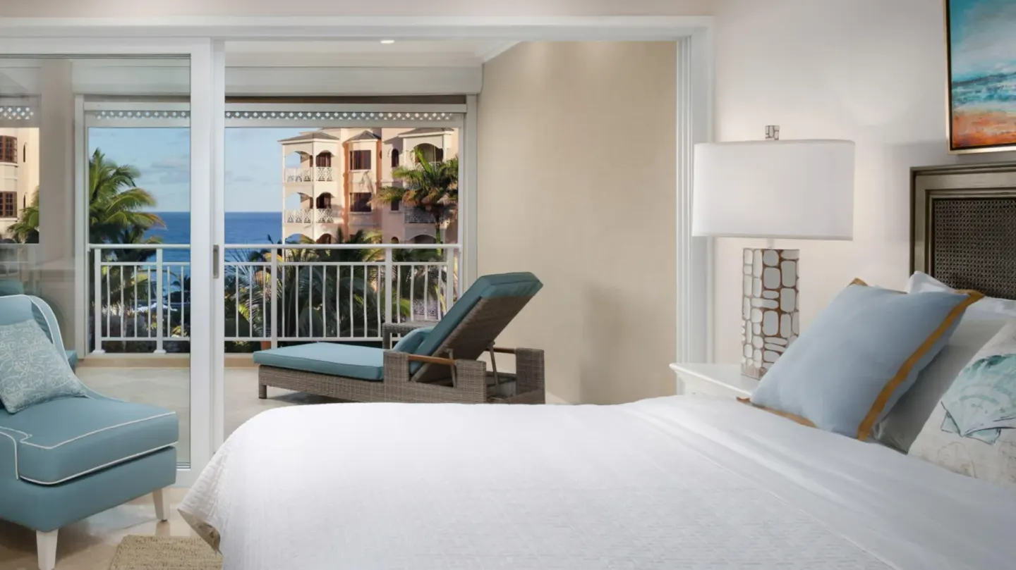 King bed beside sliding doors to a balcony with ocean glimpses at The Crane Resort.