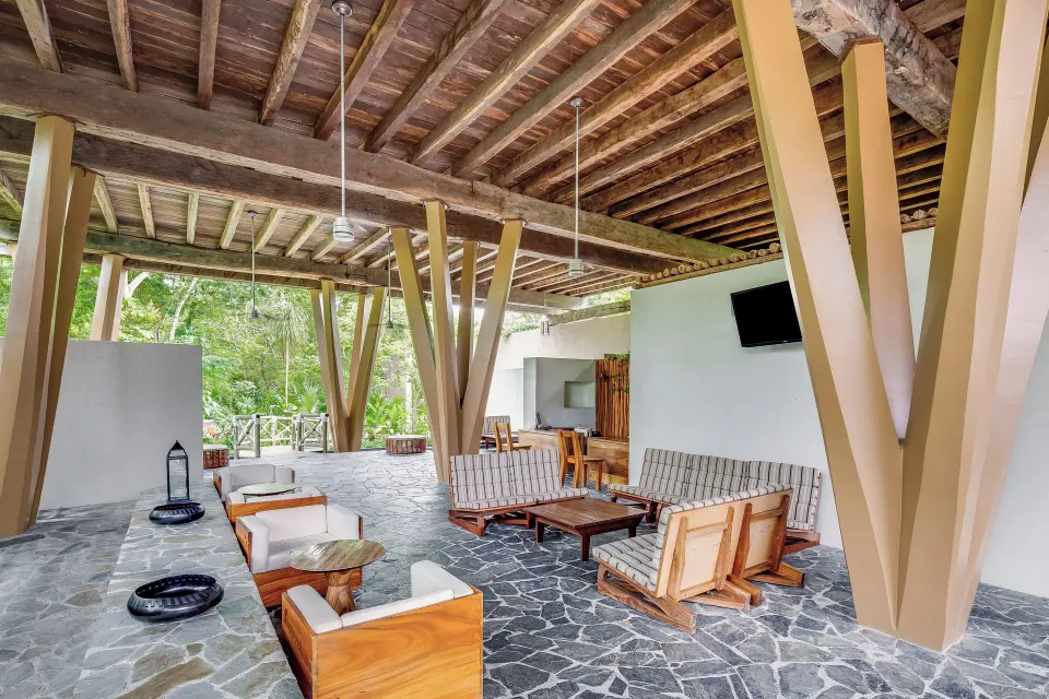 Covered communal lounge with forest views and timber beams at The Explorean Cozumel