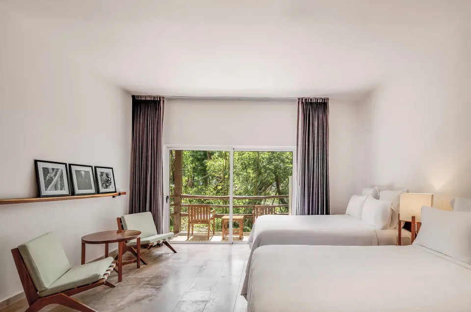 Bright guest room with two beds and a balcony view of trees at The Explorean Cozumel