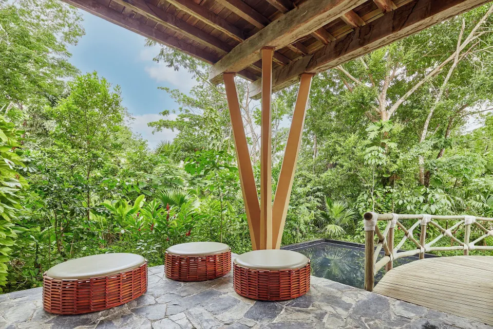 Elevated terrace with round wicker stools and dense tropical foliage at The Explorean Cozumel