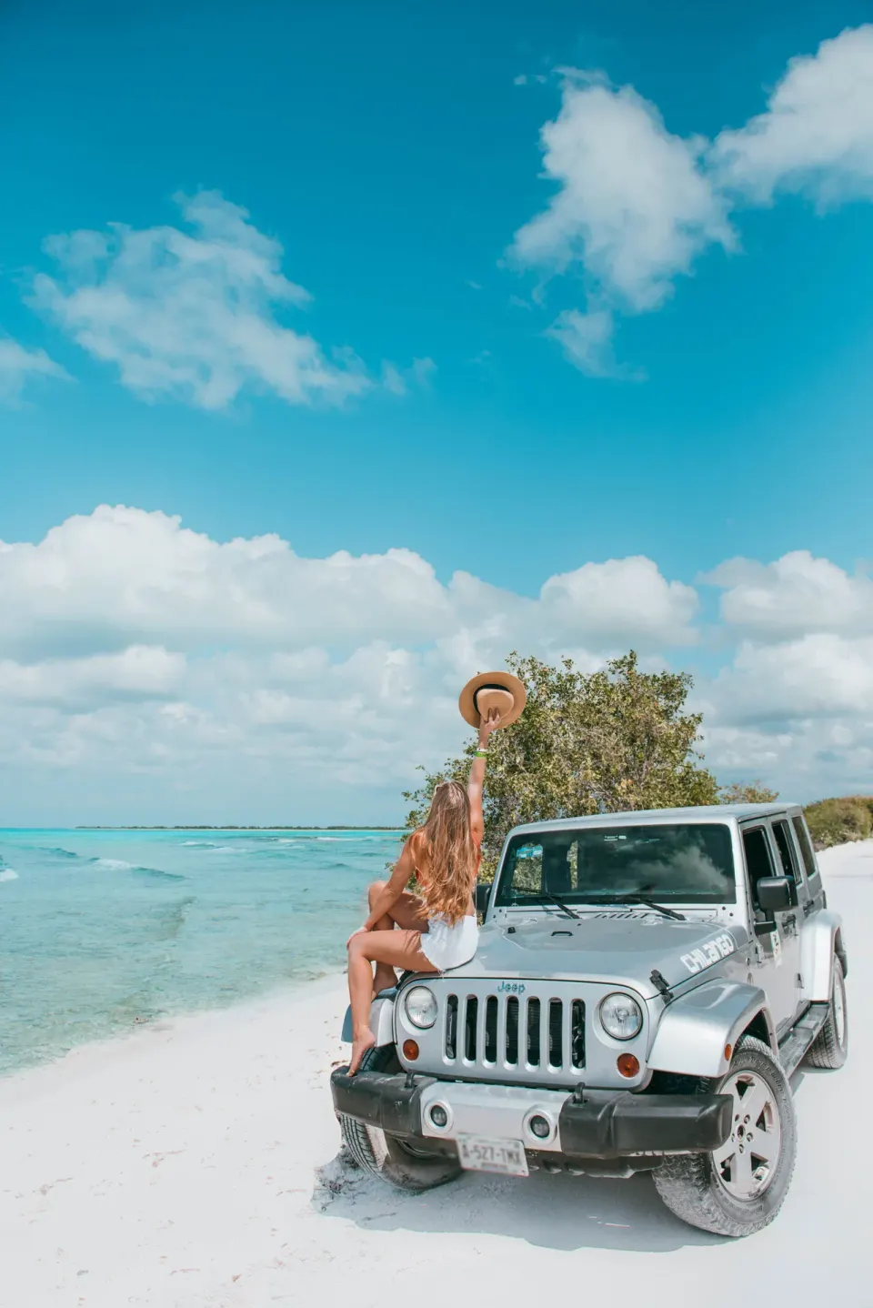 Woman sitting on a parked jeep on a white sand beach at The Explorean Cozumel