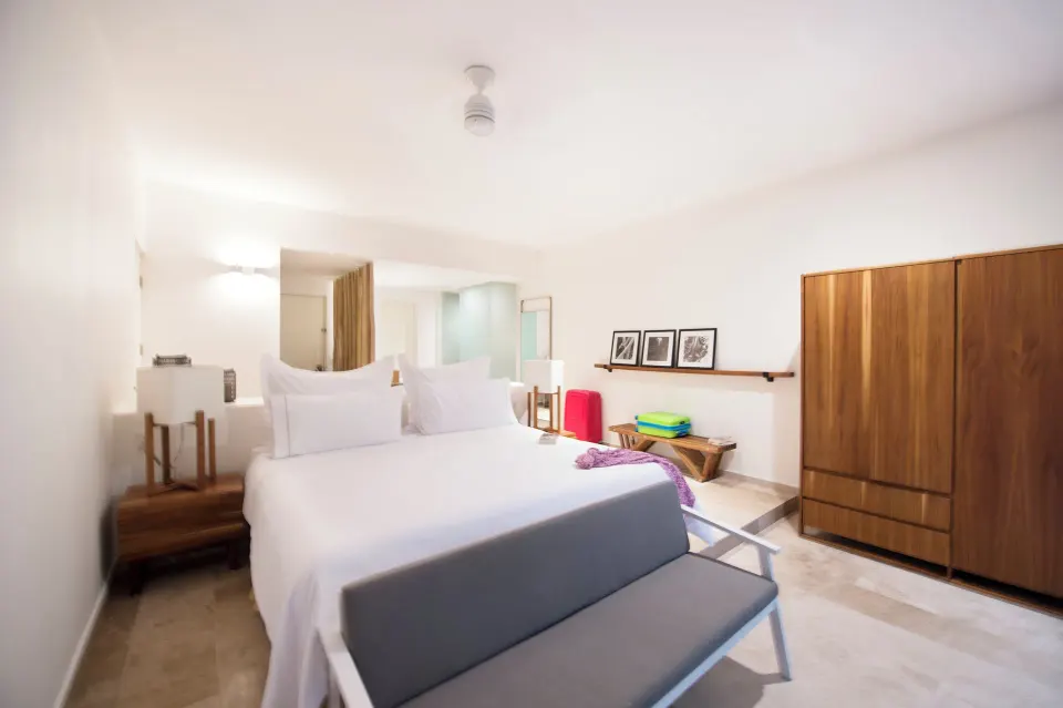 Bright king bedroom with bench at foot of bed and wardrobe at The Explorean Cozumel