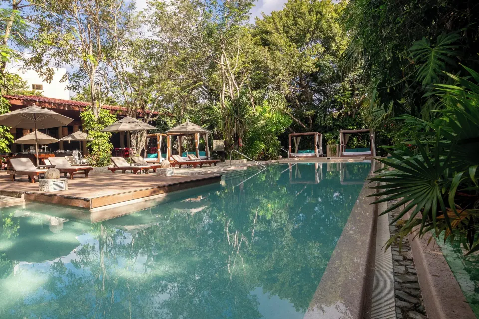 Long turquoise pool with wooden deck, loungers and cabanas surrounded by trees at The Explorean Cozumel