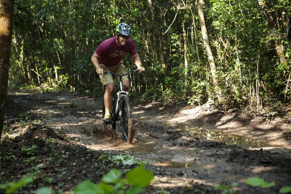 Guest mountain biking through a muddy jungle trail at The Explorean Cozumel.