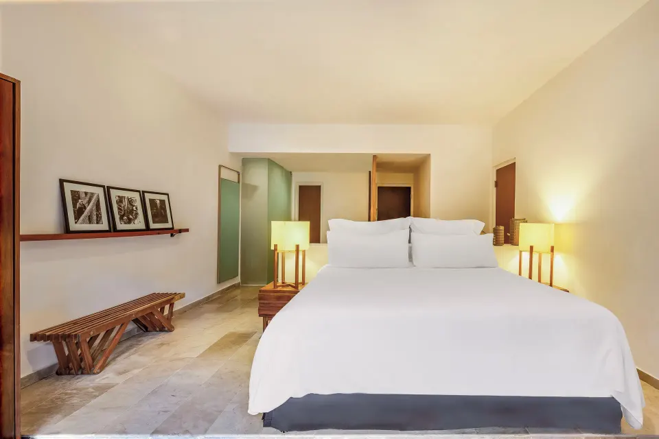 Bed with bedside lamps and rustic bench along the wall at The Explorean Cozumel