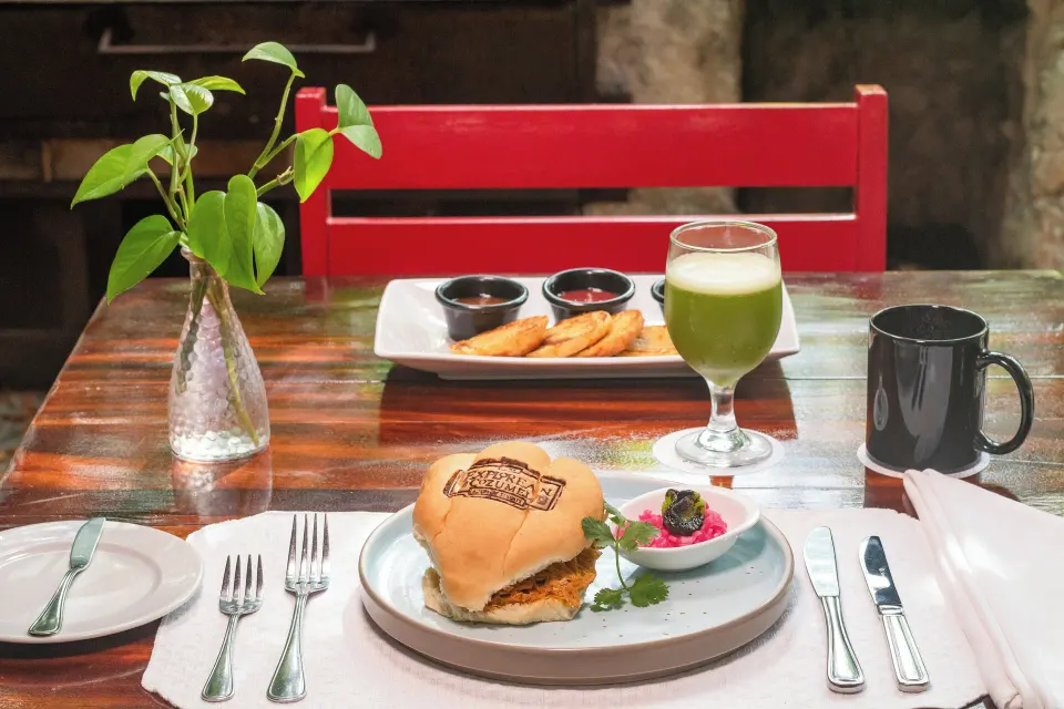 Burger, green juice and side dishes on a wooden table at The Explorean Cozumel
