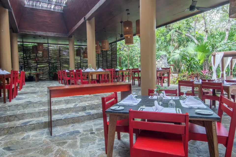 Covered open restaurant with red chairs and stone steps at The Explorean Cozumel