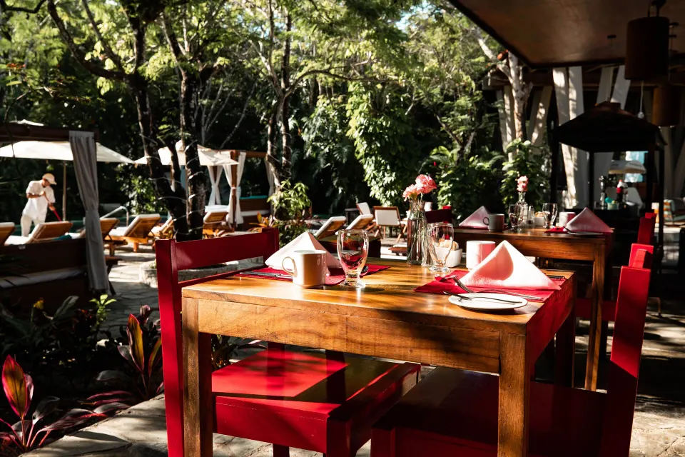 Outdoor poolside dining table with red chairs and canopy loungers at The Explorean Cozumel