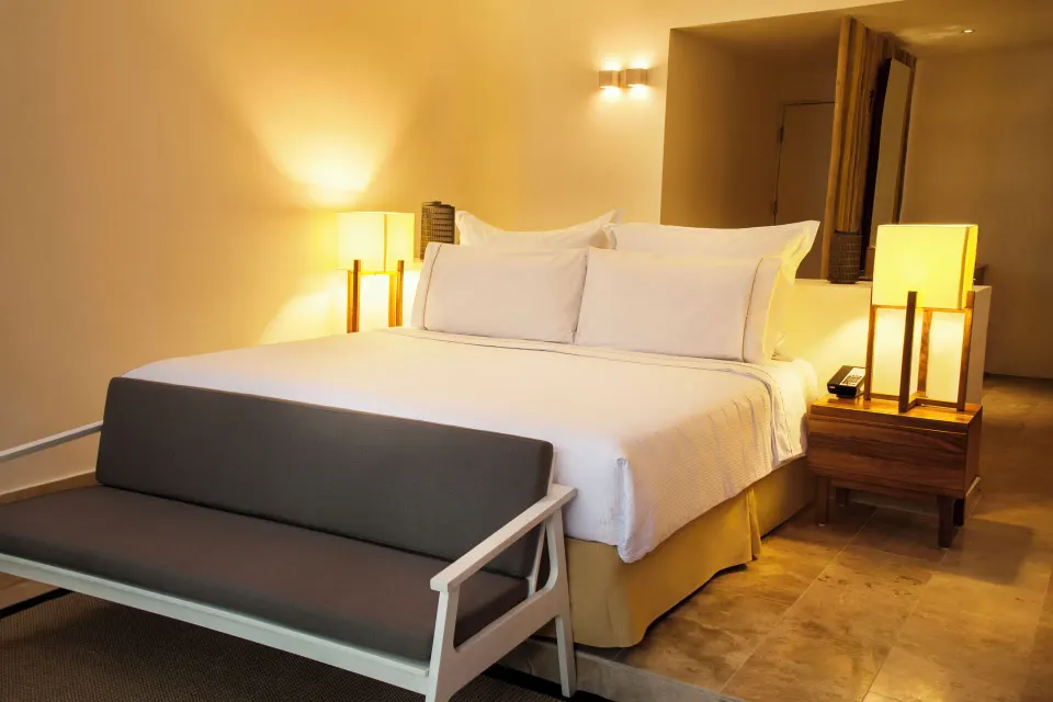 Casita king bed with bench and bedside lamps at The Explorean Cozumel