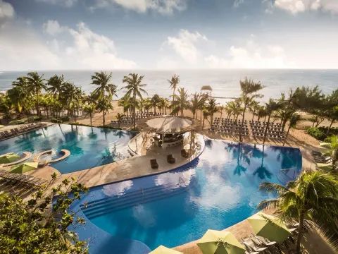 Aerial view of beachfront pools, palms, loungers, and ocean at The Fives Beach Hotel.