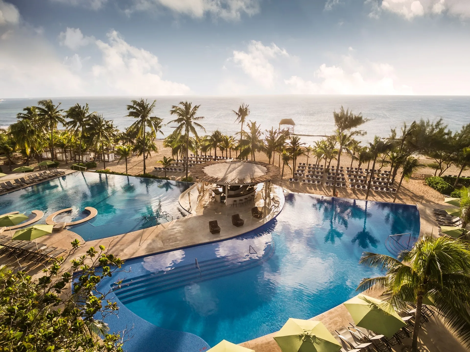 Aerial view of beachfront pools, palms, loungers, and ocean at The Fives Beach Hotel.