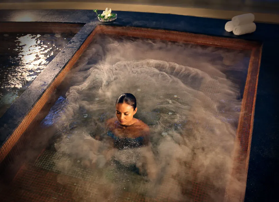 A guest sits in a bubbling spa tub with towels nearby at The Fives Beach Hotel.