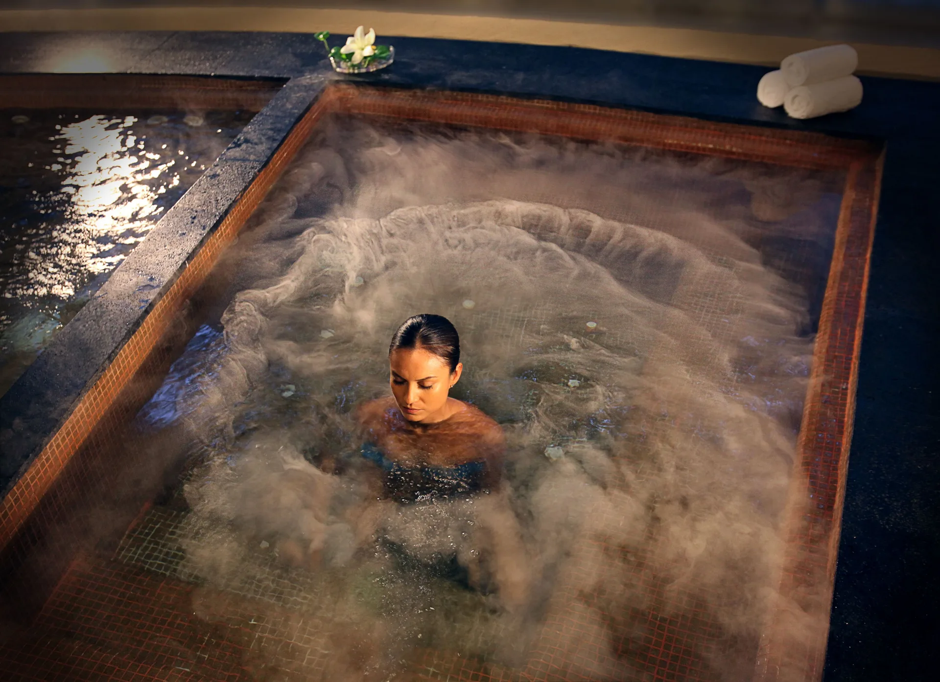 A guest sits in a bubbling spa tub with towels nearby at The Fives Beach Hotel.