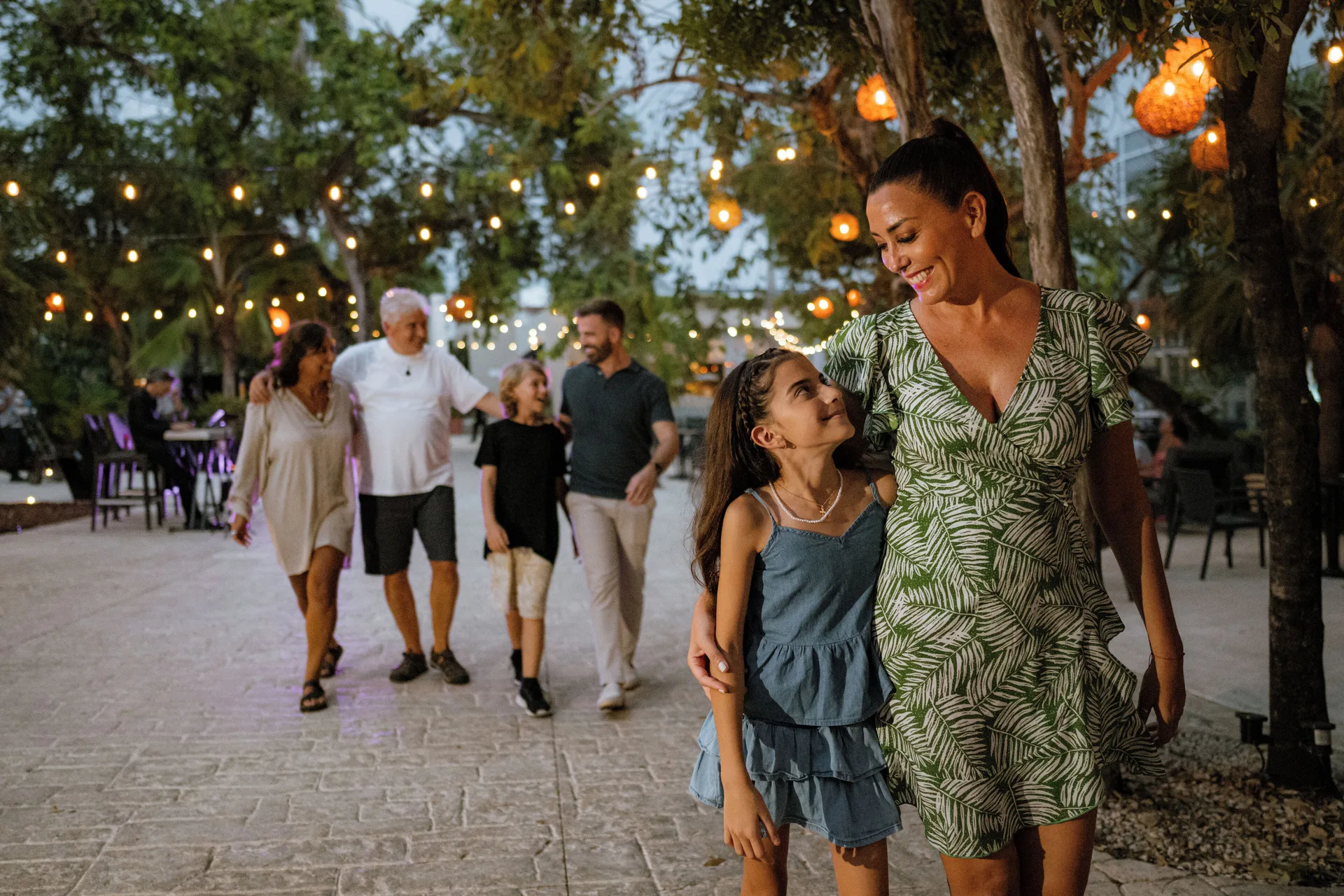Family walking under string lights on a garden path at The Fives Beach Hotel.