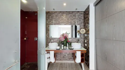 Guest bathroom with double sinks, glass shower, and red tile wall at The Fives Beach Hotel.