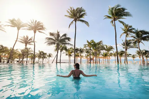 A guest relaxes in a palm-lined pool by the beach at The Fives Beach Hotel.