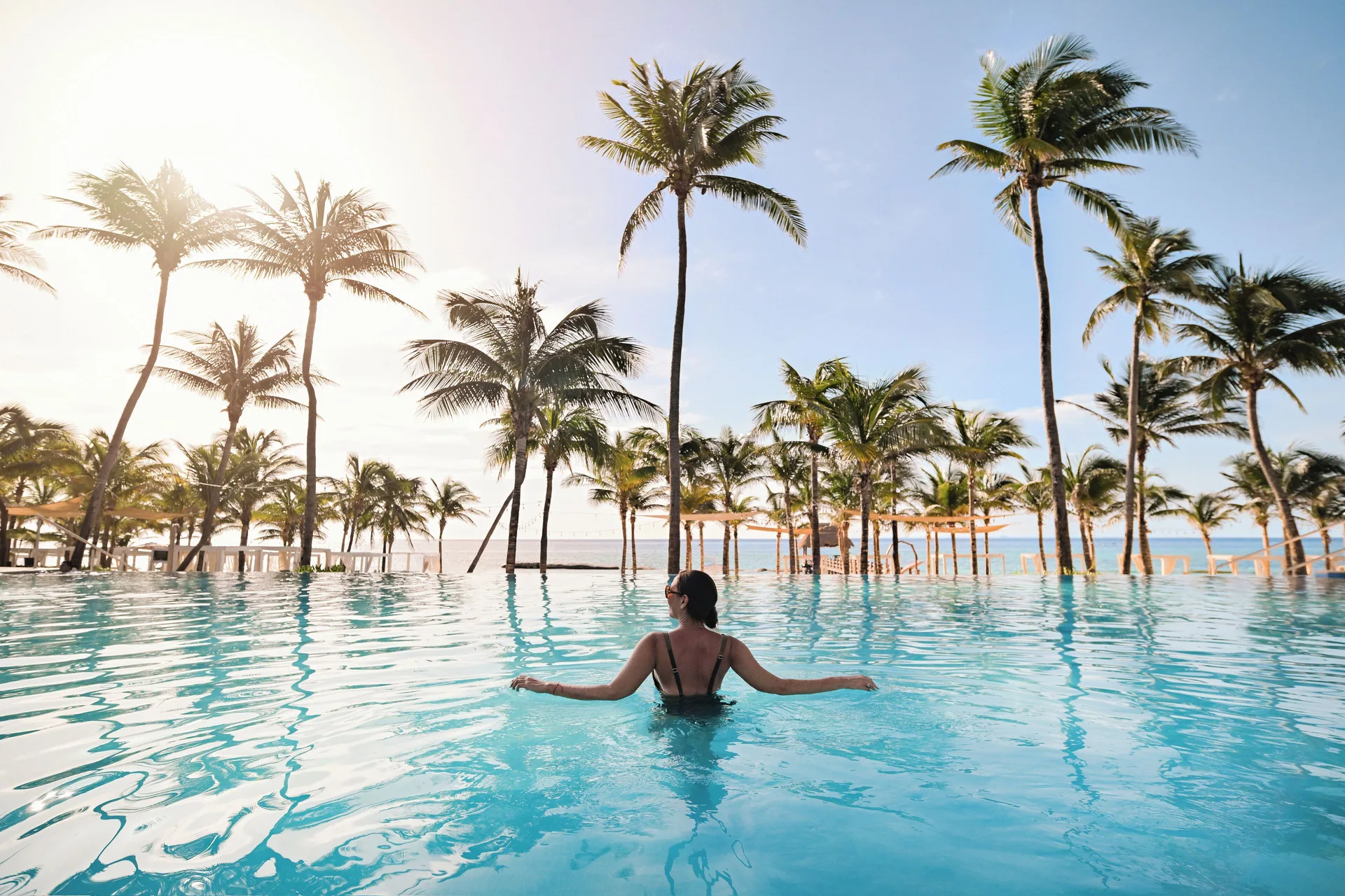 A guest relaxes in a palm-lined pool by the beach at The Fives Beach Hotel.