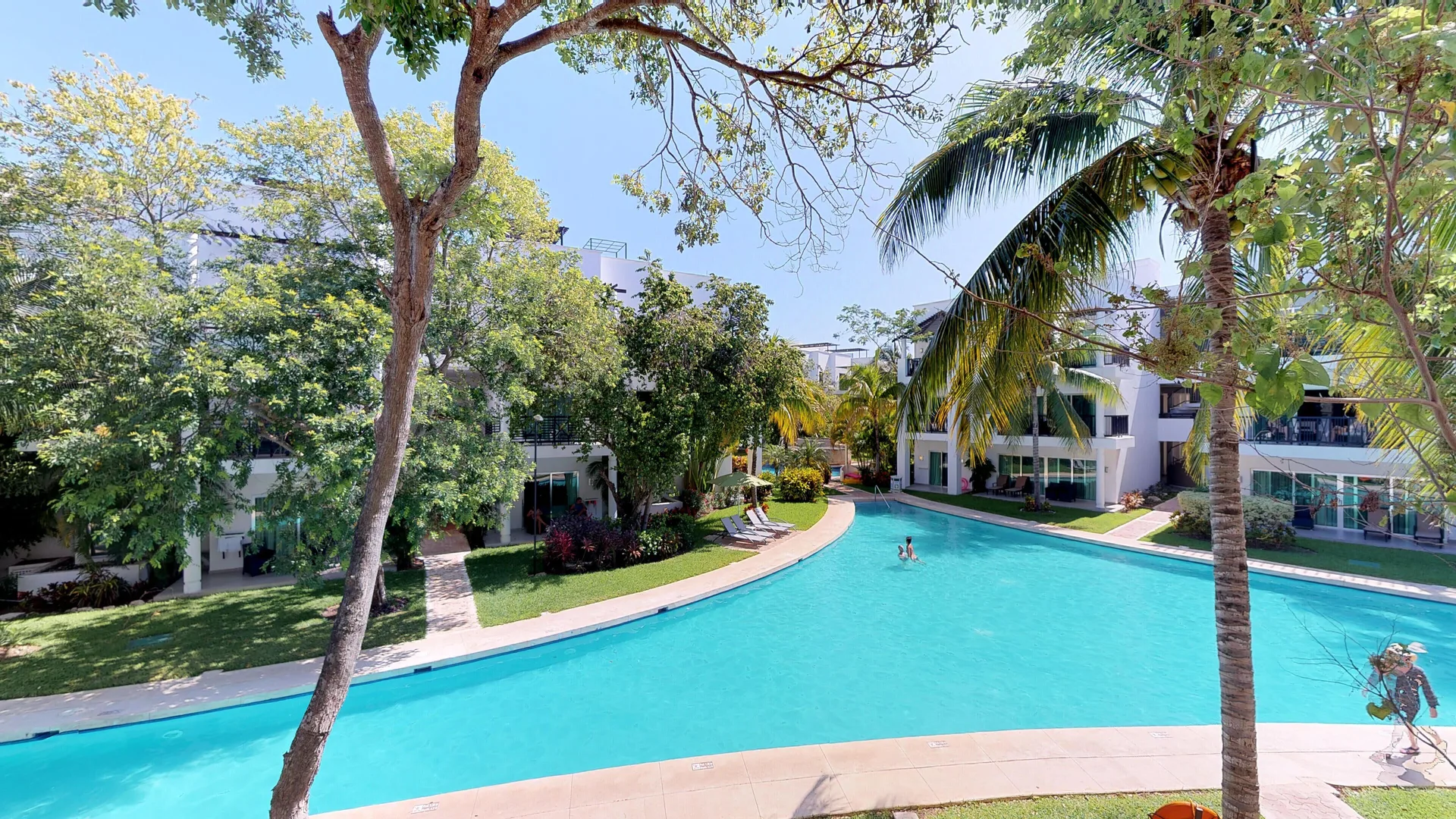 Curving pool bordered by trees and guest buildings at The Fives Beach Hotel.