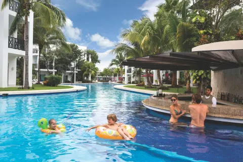 Swim-up bar and guests floating in a palm-lined pool at The Fives Beach Hotel.