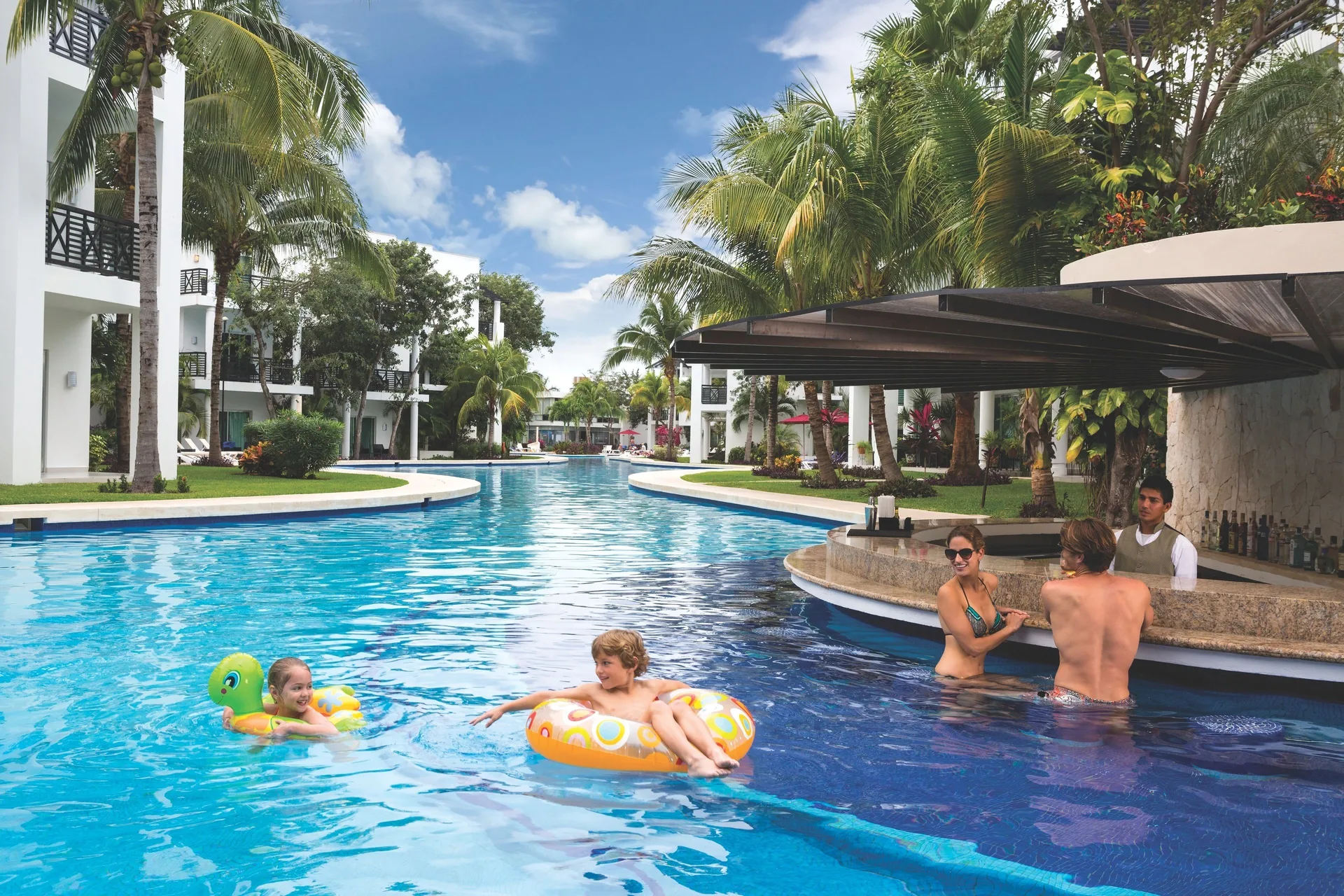 Swim-up bar and guests floating in a palm-lined pool at The Fives Beach Hotel.