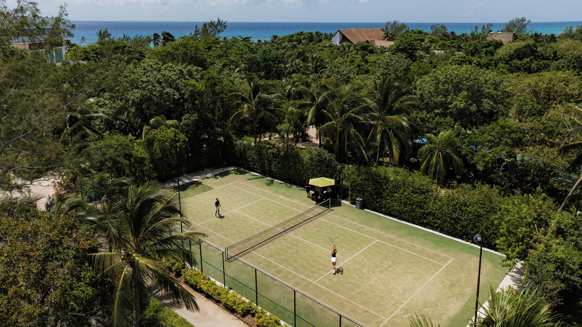 Tennis court among palms with the sea beyond at The Fives Beach Hotel.