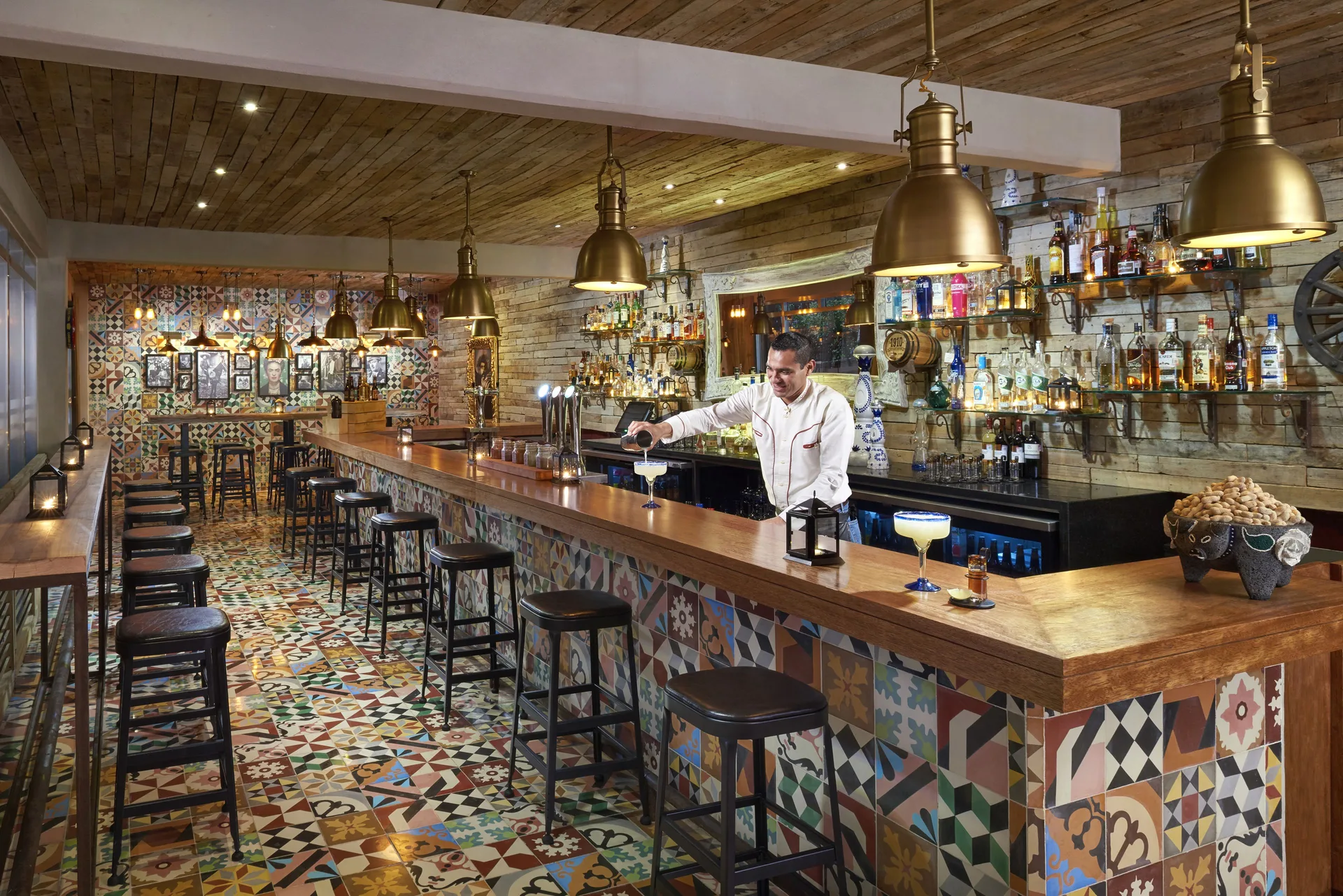 A bartender prepares cocktails behind a patterned bar at The Fives Beach Hotel.