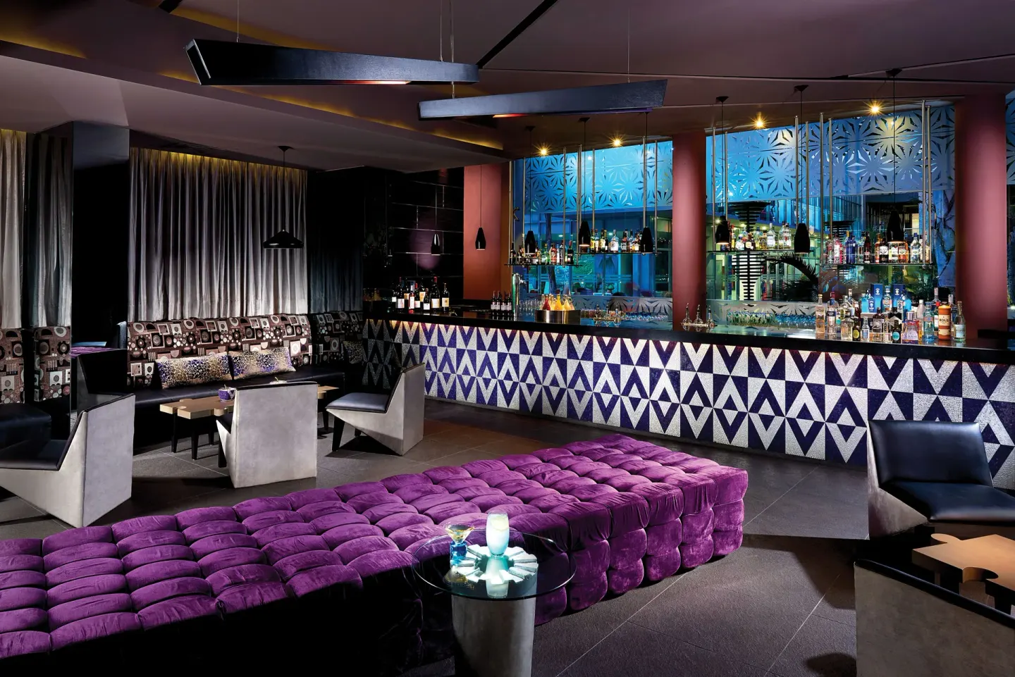 A lounge bar with purple seating and a geometric counter at The Fives Beach Hotel.