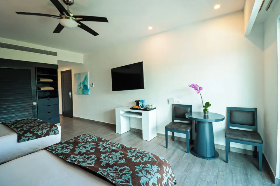 Deluxe Room with two beds, round table, chairs and TV at The Fives Beach Hotel.