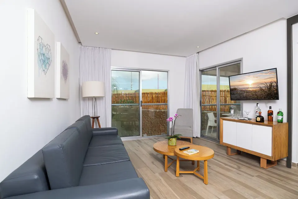 Two Bedroom Suite living room with sofa, TV, and balcony doors at The Fives Beach Hotel.