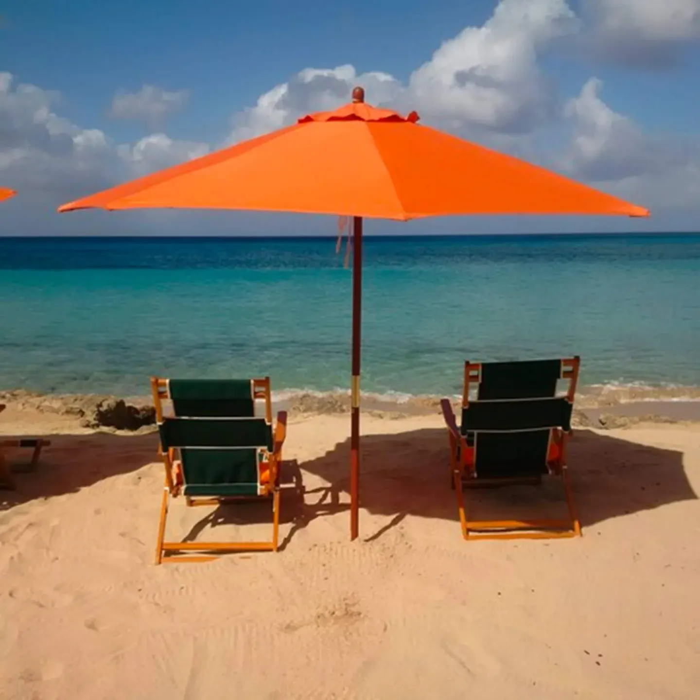 Two beach chairs sit under an orange umbrella facing the sea at The Fred.