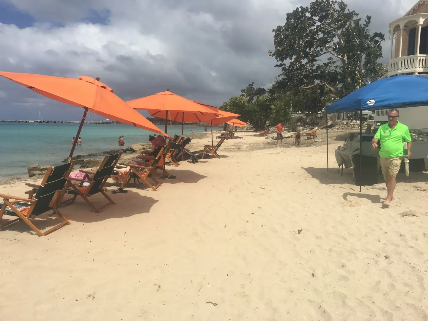 Beach at The Fred with orange umbrellas, lounge chairs, a blue canopy, and shoreline seating.