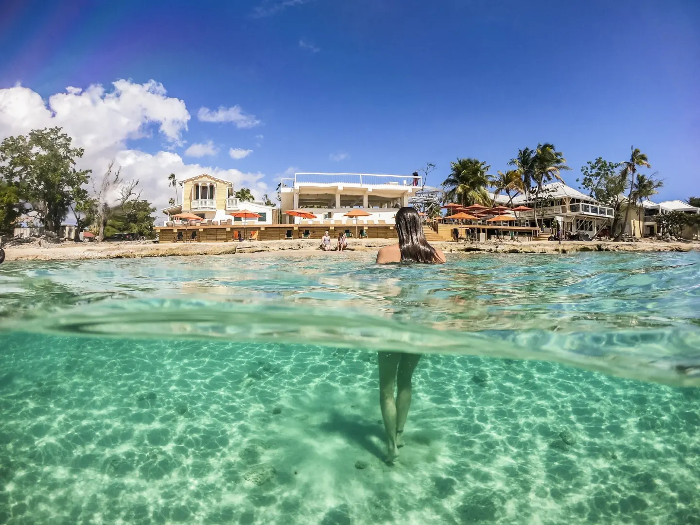Clear shallow water in front of The Fred with a swimmer facing the beach buildings.